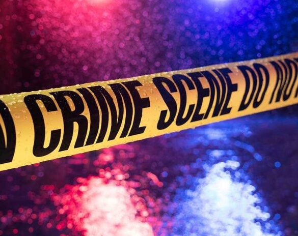 Yellow crime scene tape with police lights in background.