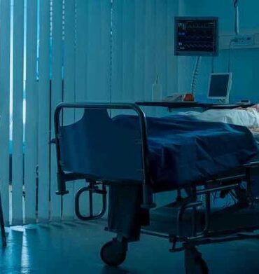 Woman sitting beside hospital bed at night.