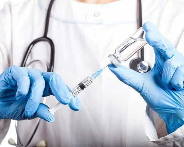 Doctor filling syringe with vaccine from vial.