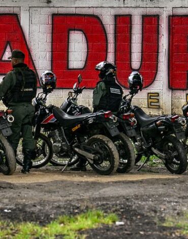 Members of the National Guard stand guard in front of a mural of ousted Venezuela's President Nicolas Maduro in Caracas on January 10, 2026. The US State Department on January 10, urged Americans in Venezuela to leave the country "immediately," citing risks from armed militias searching vehicles for US citizens at roadblocks. (Photo by Juan BARRETO / AFP via Getty Images)