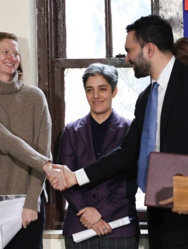 Zohran Mamdani and Cea Weaver shaking hands, with a woman in a purple jacket smiling between them.