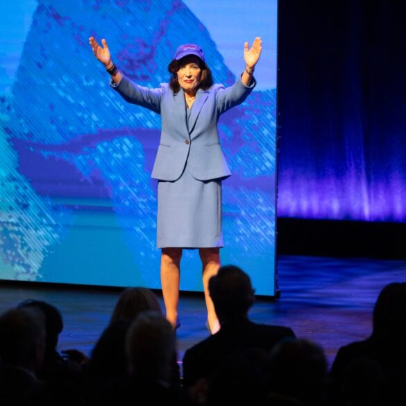 Governor Kathy Hochul, in a blue suit and hat, addresses the New York State of the State.