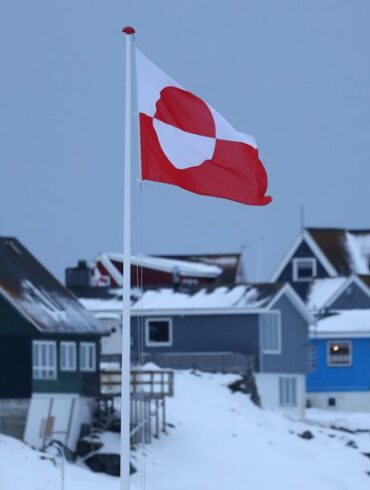 NUUK, GREENLAND - JANUARY 17: The Greenlandic flag flies over houses on January 17, 2026 in Nuuk, Greenland. Greenlandic, Danish and other European leaders are hoping they can still avert an intervention by the United States to forcefully acquire the island as U.S. President Donald Trump continues to insist the U.S. must have Greenland, suggesting even by military means if necessary. (Photo by Sean Gallup/Getty Images)