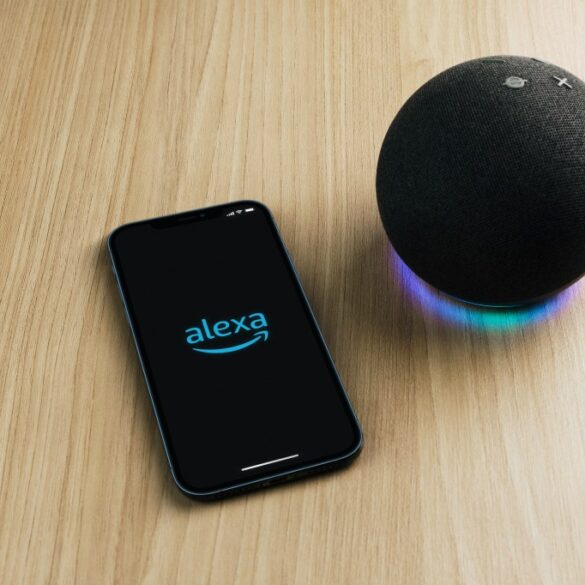 Amazon Alexa smart speaker next to a smartphone with the Alexa app open.
