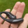 Shokz Openfit Pro outside, outside held in a woman's hand, with green grass in the background