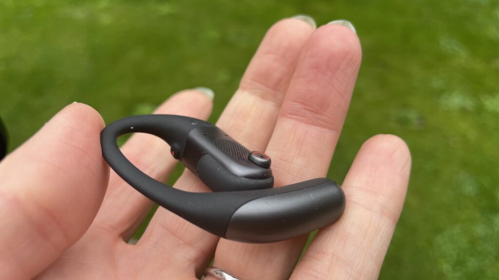 Shokz Openfit Pro outside, outside held in a woman's hand, with green grass in the background