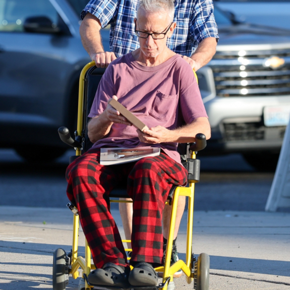 Andy Dick in a wheelchair, being pushed by a companion, on an afternoon outing in Los Angeles.