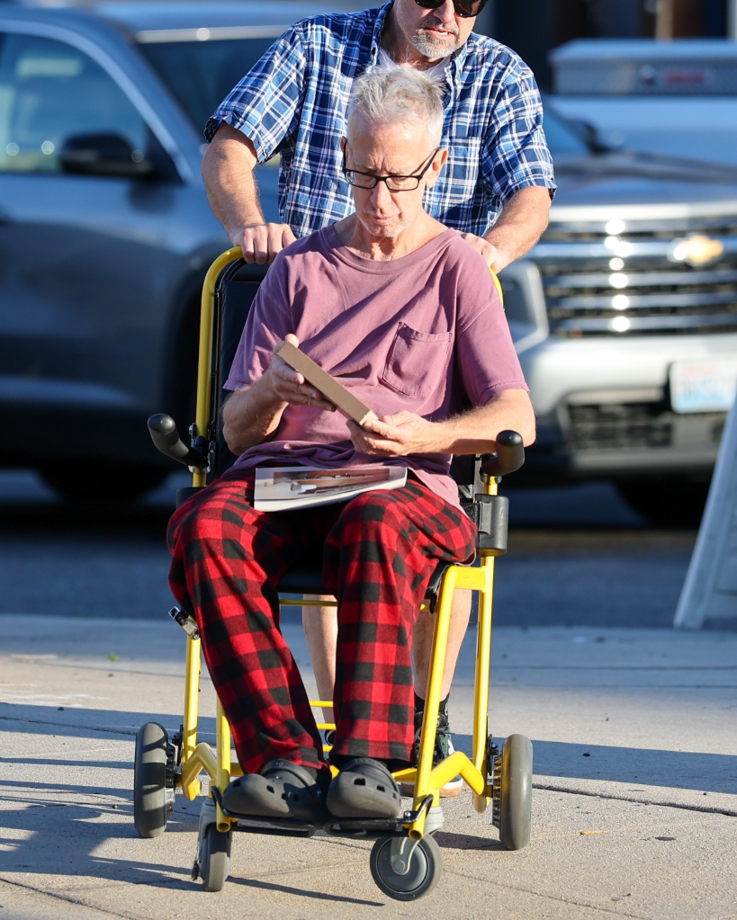 Andy Dick in a wheelchair, being pushed by a companion, on an afternoon outing in Los Angeles.
