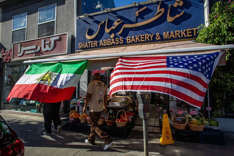 A man walks by a Iranian Market with an Iranian and an American flag outsite the shop in the Persian Square at the West LA neighborhood with in Los Angeles, California on February 28, 2026. The US and Israel launched an attack of unprecedented scale against Iran on Saturday, reportedly killing more than 200 people, with Tehran launching a retaliatory missile barrage that sent people running for cover across the Middle East. (Photo by Apu GOMES / AFP via Getty Images)