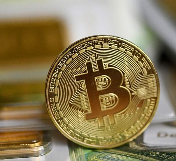 100g gold bullion bars of the German precious metals trading company Degussa (Deutsche Gold- und Silber-Scheide-Anstalt - German Gold and Silver Refining) are pictured with a commemorative Bitcoin coin on 100 euros notes in Dortmund, western Germany on February 9, 2026. (Photo by Ina FASSBENDER / AFP via Getty Images)