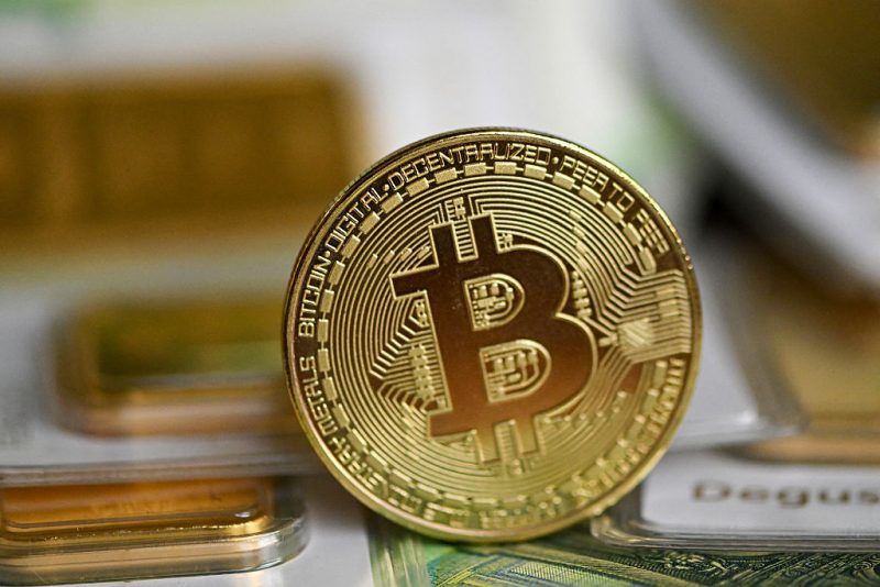 100g gold bullion bars of the German precious metals trading company Degussa (Deutsche Gold- und Silber-Scheide-Anstalt - German Gold and Silver Refining) are pictured with a commemorative Bitcoin coin on 100 euros notes in Dortmund, western Germany on February 9, 2026. (Photo by Ina FASSBENDER / AFP via Getty Images)