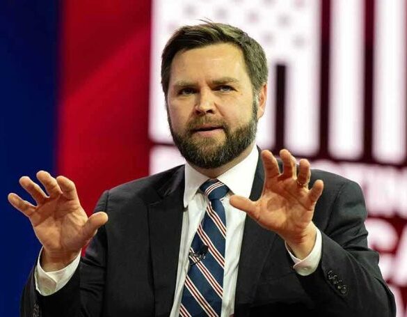 Man in suit gesturing with hands on stage.