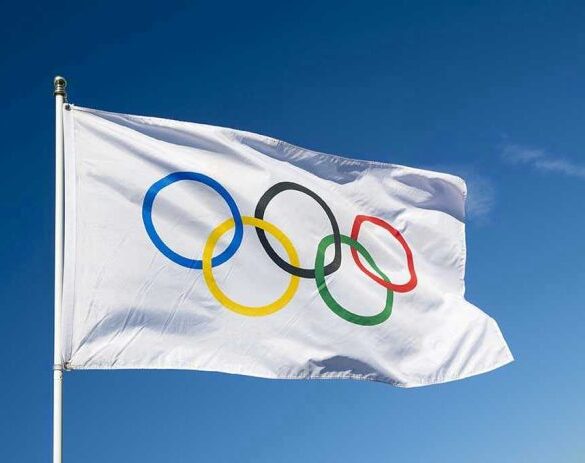 Olympic flag waving against clear blue sky.