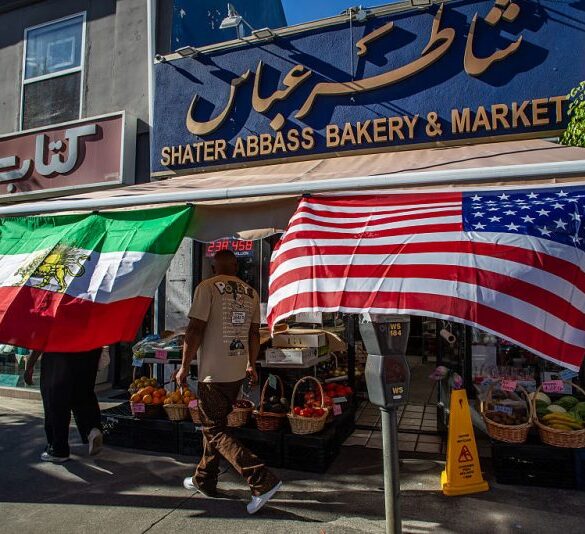 A man walks by a Iranian Market with an Iranian and an American flag outsite the shop in the Persian Square at the West LA neighborhood with in Los Angeles, California on February 28, 2026. The US and Israel launched an attack of unprecedented scale against Iran on Saturday, reportedly killing more than 200 people, with Tehran launching a retaliatory missile barrage that sent people running for cover across the Middle East. (Photo by Apu GOMES / AFP via Getty Images)