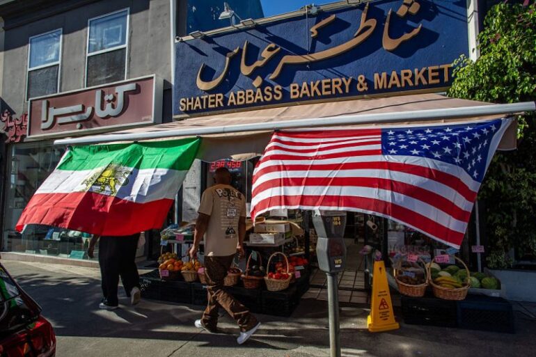 A man walks by a Iranian Market with an Iranian and an American flag outsite the shop in the Persian Square at the West LA neighborhood with in Los Angeles, California on February 28, 2026. The US and Israel launched an attack of unprecedented scale against Iran on Saturday, reportedly killing more than 200 people, with Tehran launching a retaliatory missile barrage that sent people running for cover across the Middle East. (Photo by Apu GOMES / AFP via Getty Images)