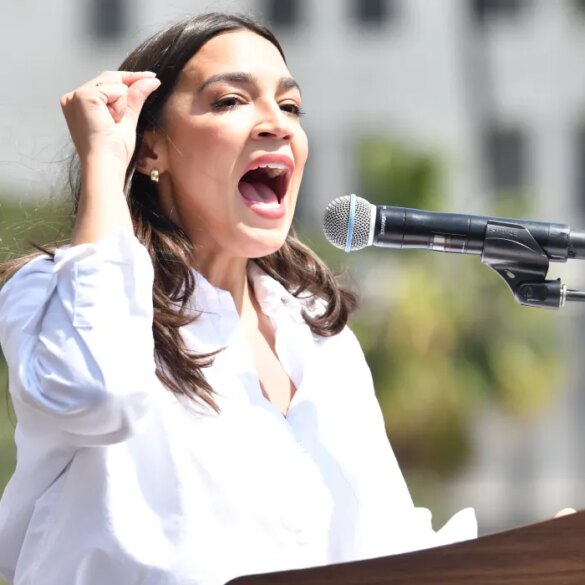 Congresswoman Alexandria Ocasio-Cortez speaking into a microphone at the "Fighting Oligarchy" rally.