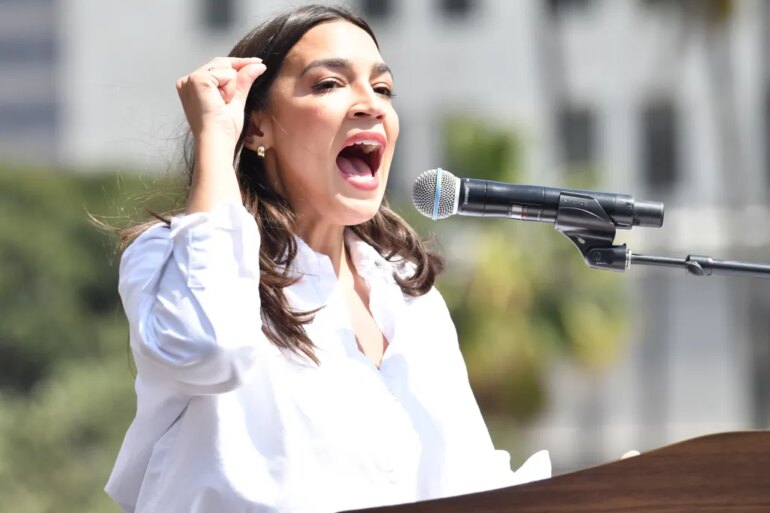 Congresswoman Alexandria Ocasio-Cortez speaking into a microphone at the "Fighting Oligarchy" rally.