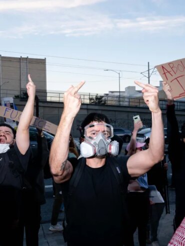 Protesters hold signs that read "Impeach Trump" and "Abolish ICE" while giving the middle finger.