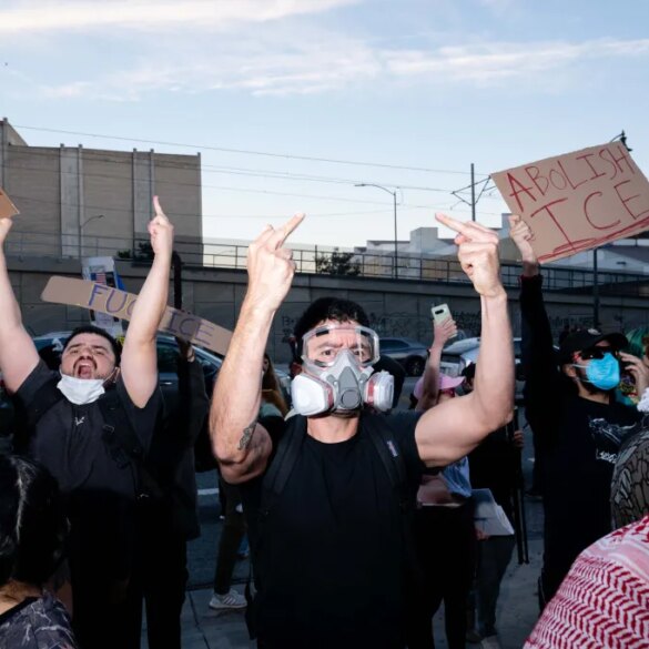 Protesters hold signs that read "Impeach Trump" and "Abolish ICE" while giving the middle finger.