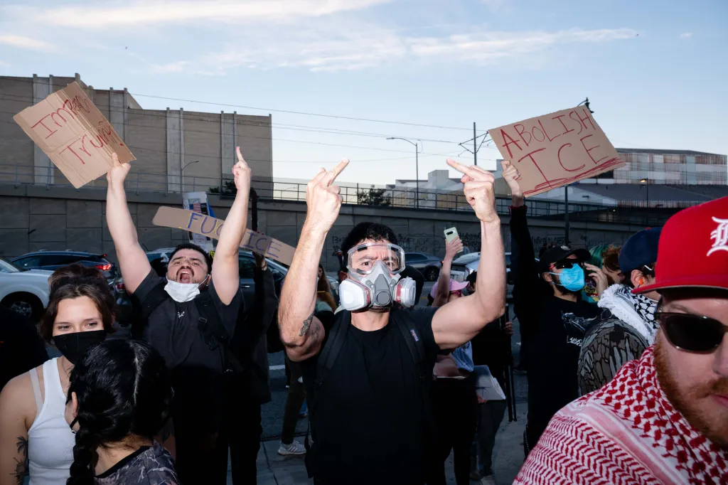 Protesters hold signs that read "Impeach Trump" and "Abolish ICE" while giving the middle finger.