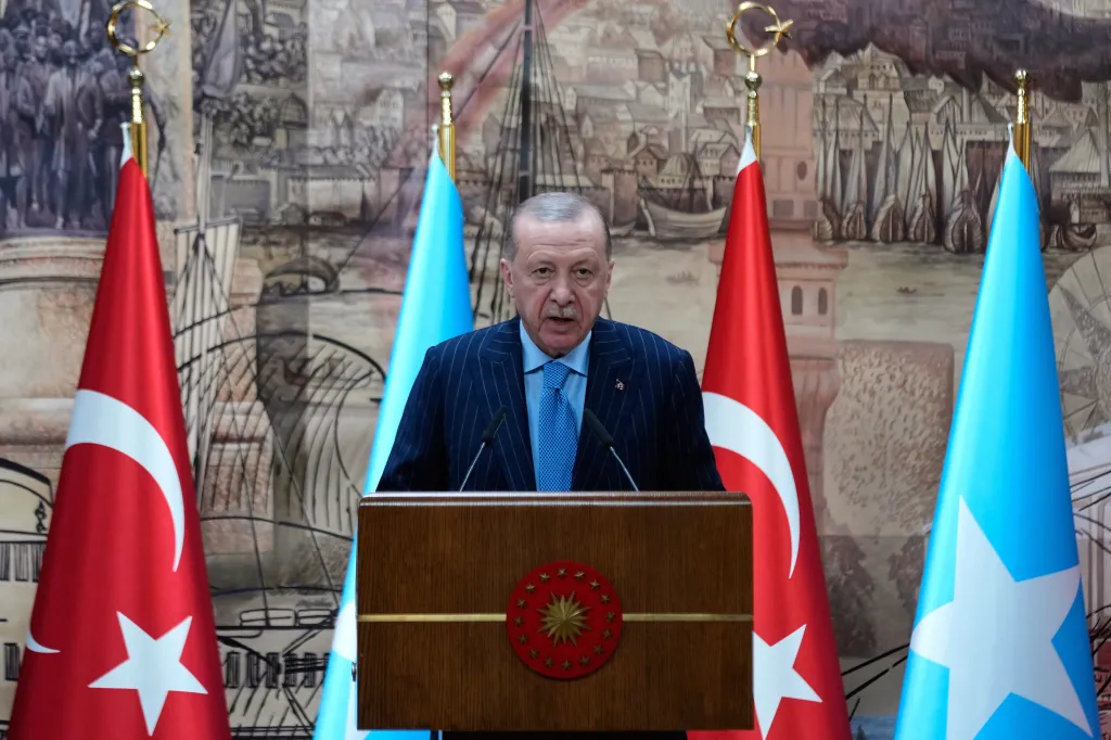 Turkish President Recep Tayyip Erdogan speaking at a podium with Turkish and Somali flags.