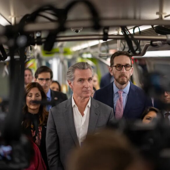California Governor Gavin Newsom on a train, surrounded by a crowd and cameras.