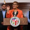 Los Angeles Mayor Karen Bass speaking at a podium with two people standing behind her.
