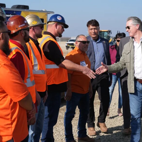 California Gov. Gavin Newsom shaking hands with an Iron Workers Local 155 worker as Ian Choudri, CEO for the California High-Speed Rail Authority, watches.