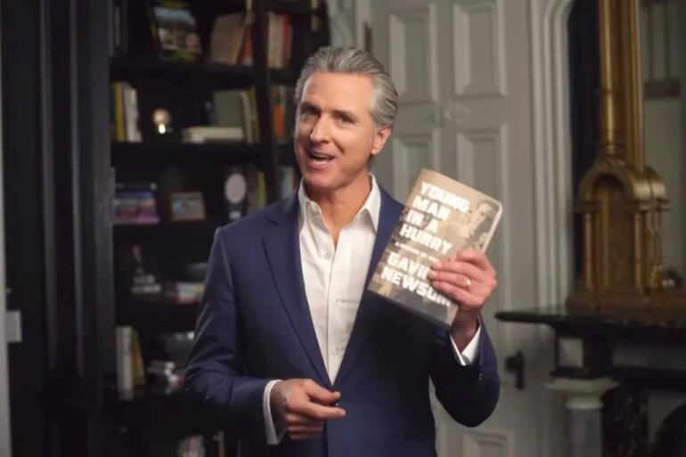 Gavin Newsom holding up his book, "Young Man in a Hurry: A Memoir of Discovery"