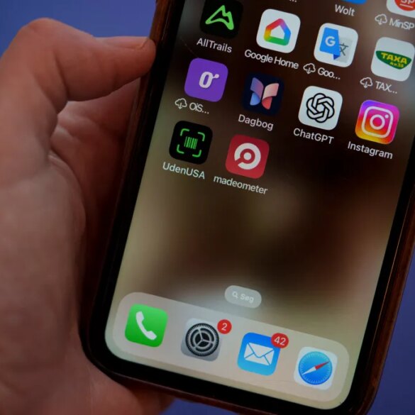A close-up of a hand holding a smartphone displaying apps, including "UdenUSA" and "Madeometer", designed to filter out American products.