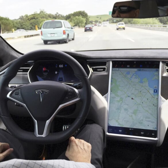 The interior of a Tesla Model S in San Francisco, showing the steering wheel and a large center screen displaying a map, with a highway visible through the windshield.