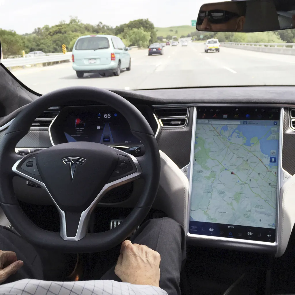 The interior of a Tesla Model S in San Francisco, showing the steering wheel and a large center screen displaying a map, with a highway visible through the windshield.