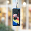 Kodak Charmera compact camera dangling from its keychain, with shop frontage backdrop