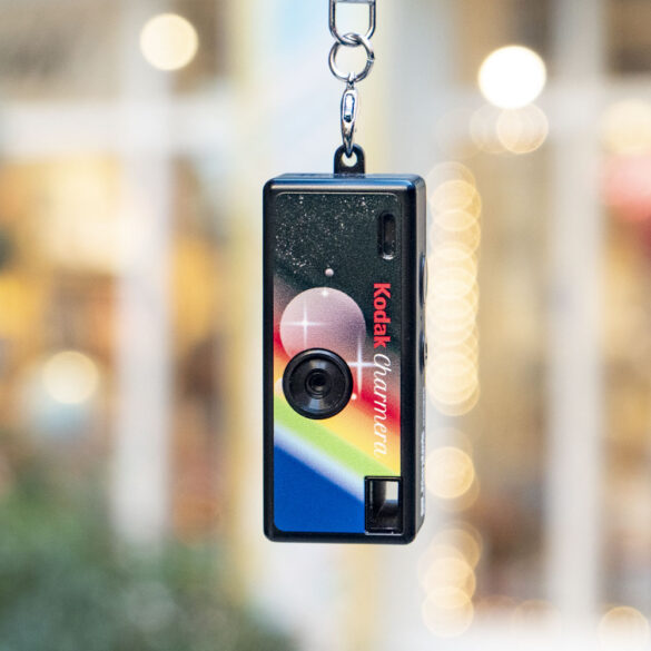 Kodak Charmera compact camera dangling from its keychain, with shop frontage backdrop