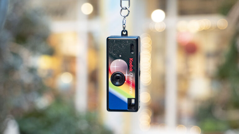 Kodak Charmera compact camera dangling from its keychain, with shop frontage backdrop