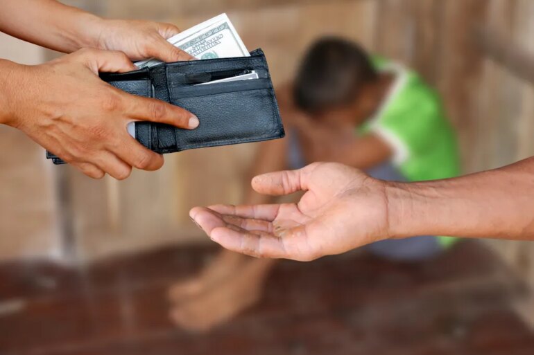 A person's hands holding a wallet full of money over another person's open, dirty hand, with a third, sad, blurred person in the background, illustrating human trafficking.