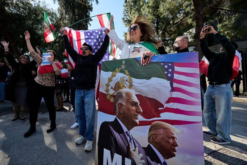 An anti-Iranian regime protestor holds a placard bearing images depicting the son of Iran's Last Shah and now key opposition figure, Reza Pahlavi and US President, Donald Trump as protestors gather in front of the Iranian Embassy in Athens on March 1, 2026, during a protest in support of the US and Israel attack on Iran and the killing of Iran's supreme leader. Iranian state television confirmed the death of Iran's supreme leader Ayatollah Ali Khamenei on February 28, 2026, after US President said he had been killed. The announcement came after the United States and Israel started launching waves of strikes against targets in Iran, sparking swift retaliation by the Islamic Republic. (Photo by Aggelos NAKKAS / AFP via Getty Images)