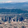 Aerial view of downtown Los Angeles with the Hollywood sign on a distant mountain and additional mountains in the background.