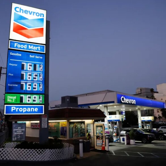 A Chevron gas station at dusk shows gas prices at $7.61 for regular, $7.65 for plus, and $7.69 for supreme gasoline, with diesel and propane also listed.