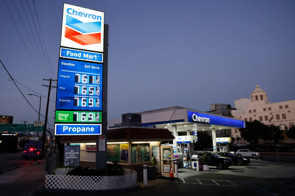 A Chevron gas station at dusk shows gas prices at $7.61 for regular, $7.65 for plus, and $7.69 for supreme gasoline, with diesel and propane also listed.