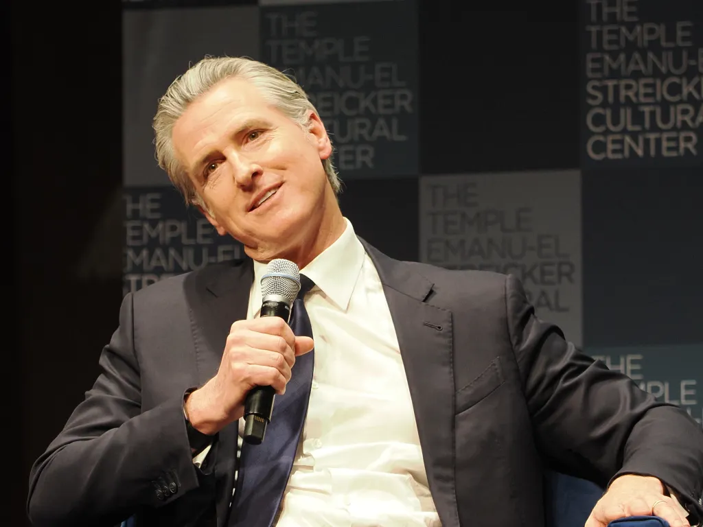 Gavin Newsom speaking at Temple Emanu-El, holding a microphone.
