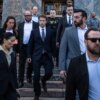 Mark Zuckerberg, in a dark suit, walks down courthouse steps surrounded by security.