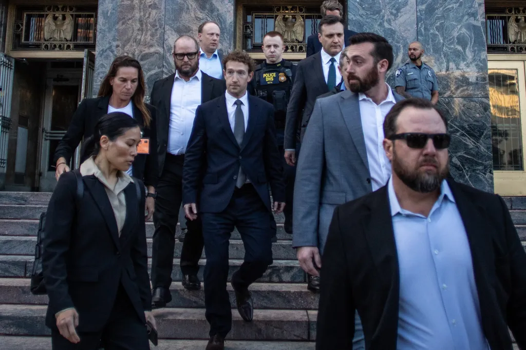 Mark Zuckerberg, in a dark suit, walks down courthouse steps surrounded by security.